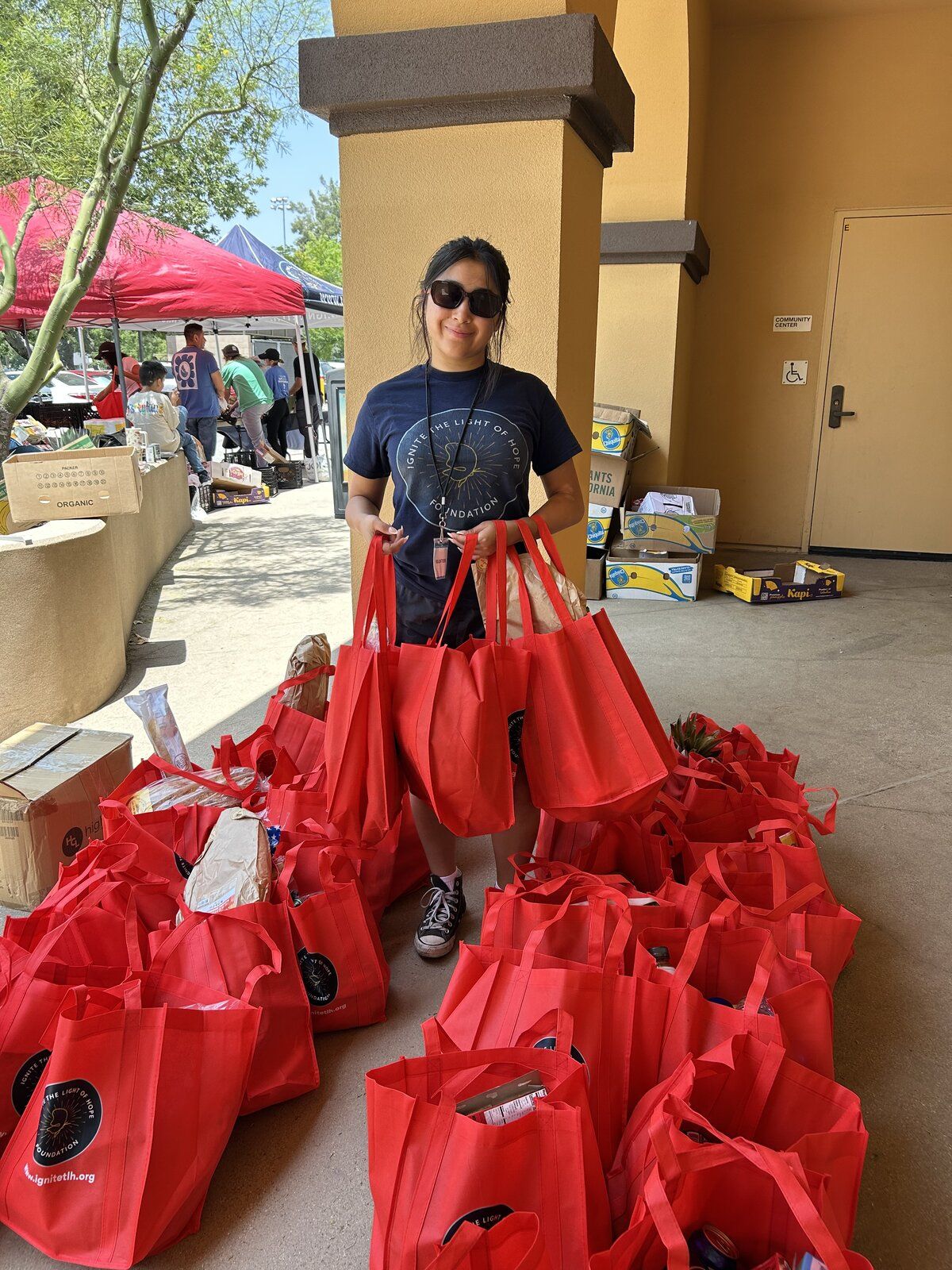 A volunteer with rows of red Ignite tote bags packed with groceries for Bags of Hope delivery